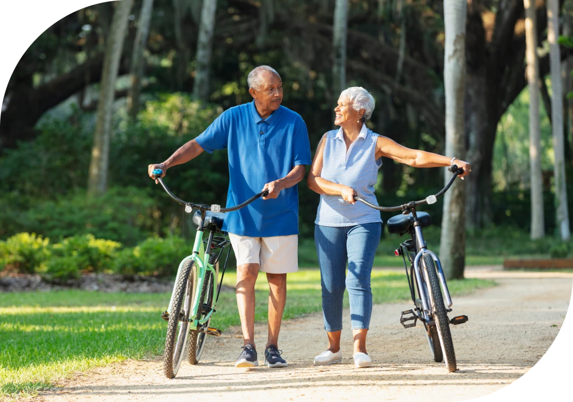 Older couple walking with bicycles in park.