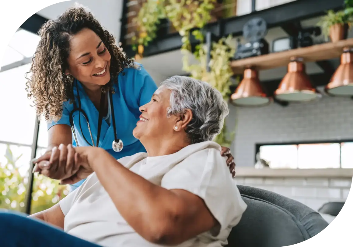 A caregiver warmly holding hands with an elderly woman at home.