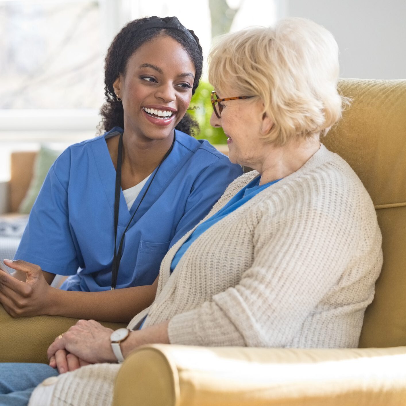A nurse warmly chatting with an elderly woman in a cozy living room.