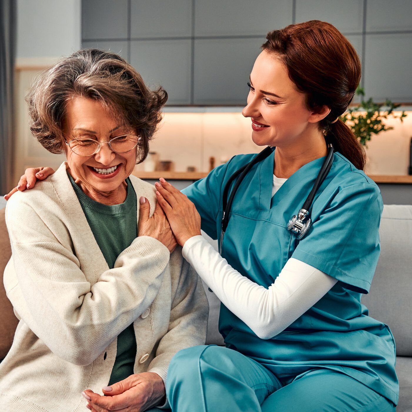 A nurse warmly comforts an elderly woman in a home setting.